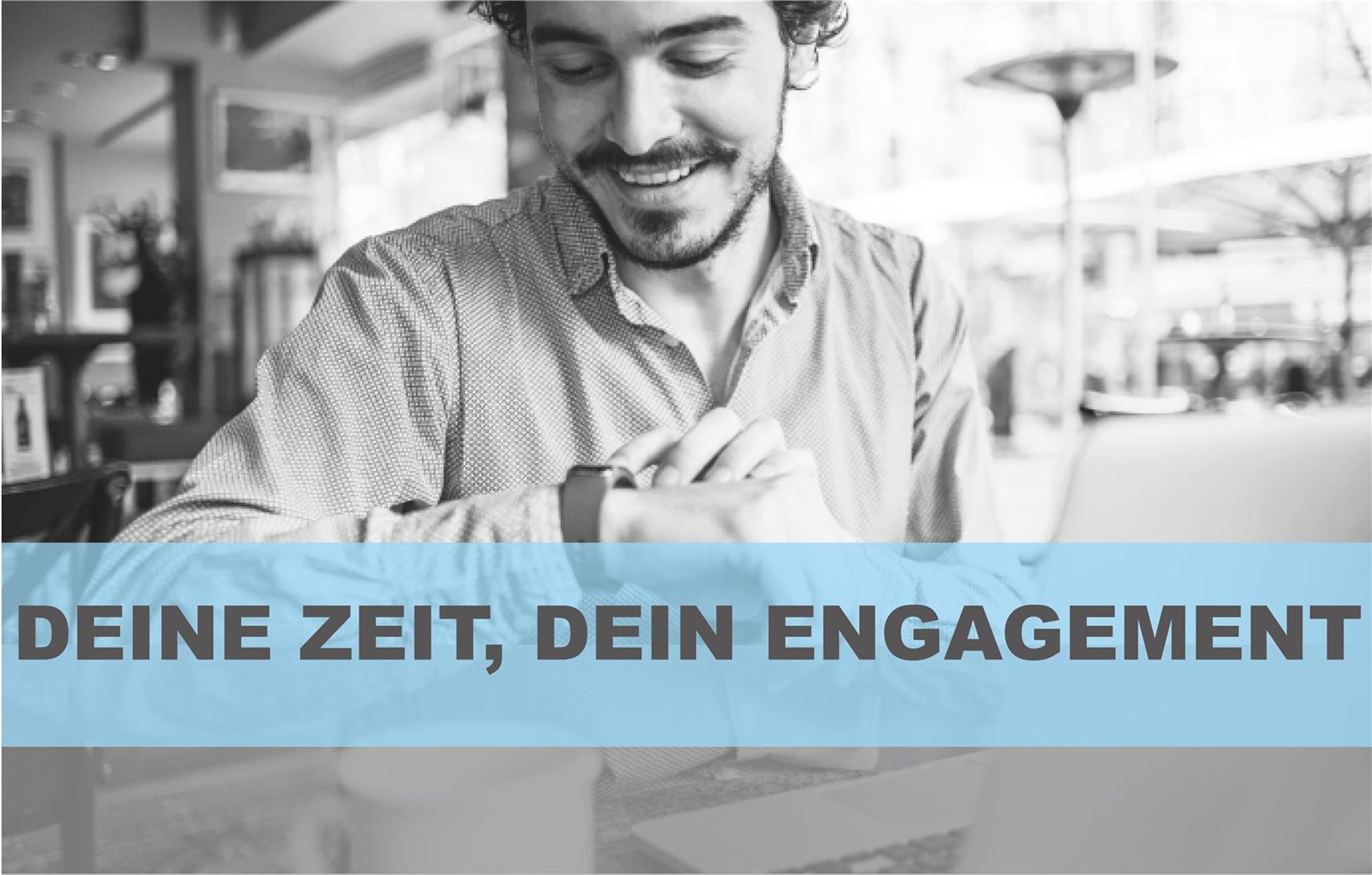 Ein Mann sitzt in einem Kaffee und schaut auf die Uhr, er lächelt dabei